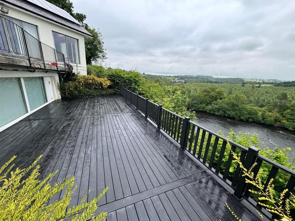 A raised composite deck in dark grey with matching railings, overlooking a river and wooded valley.