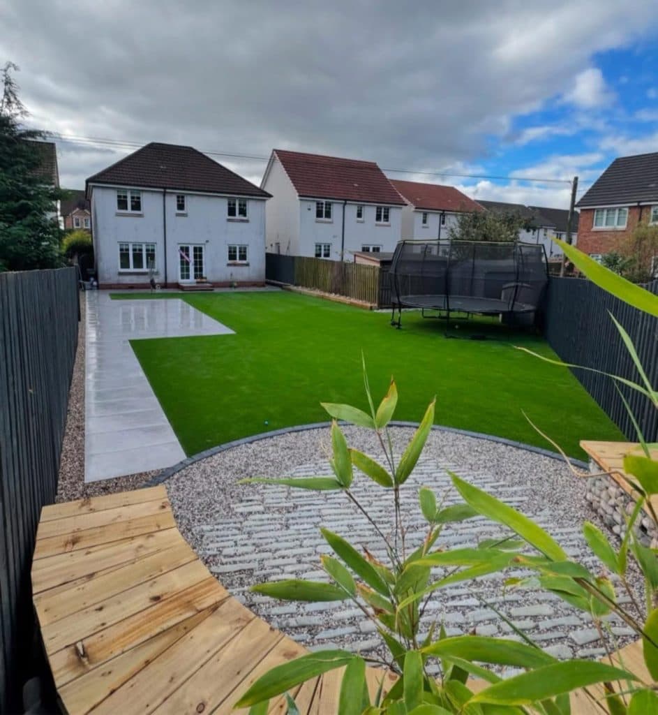 A family garden with a large lawn, a cobbled circle feature and a curved timber seating deck.