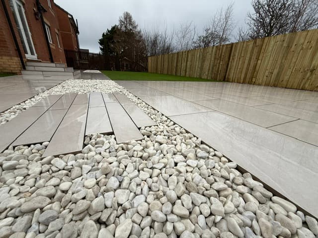 Large pale porcelain slabs laid beside a wide border of white pebbles, running along a new close-board fence.